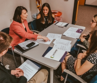 An adult sitting at a table with high school age children explaining paperwork 